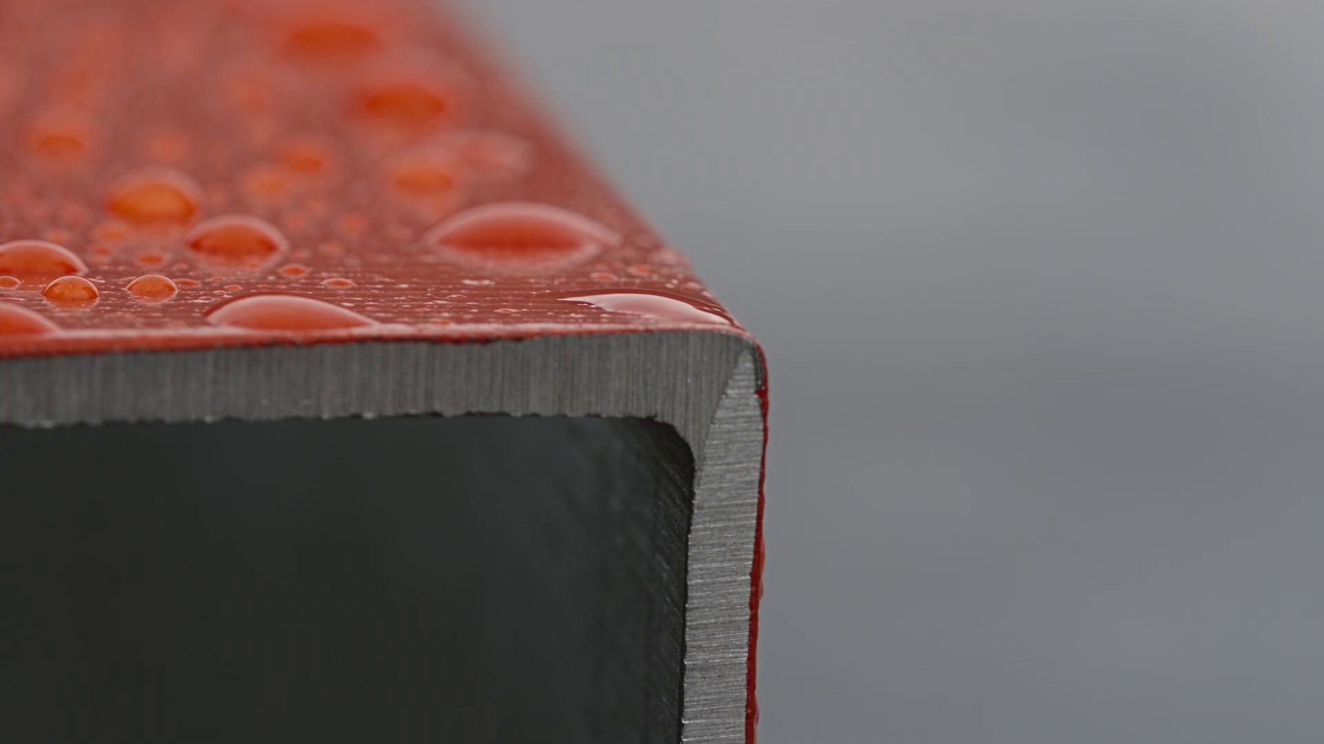 Raindrops on the red-lacquered edge of a steel section.